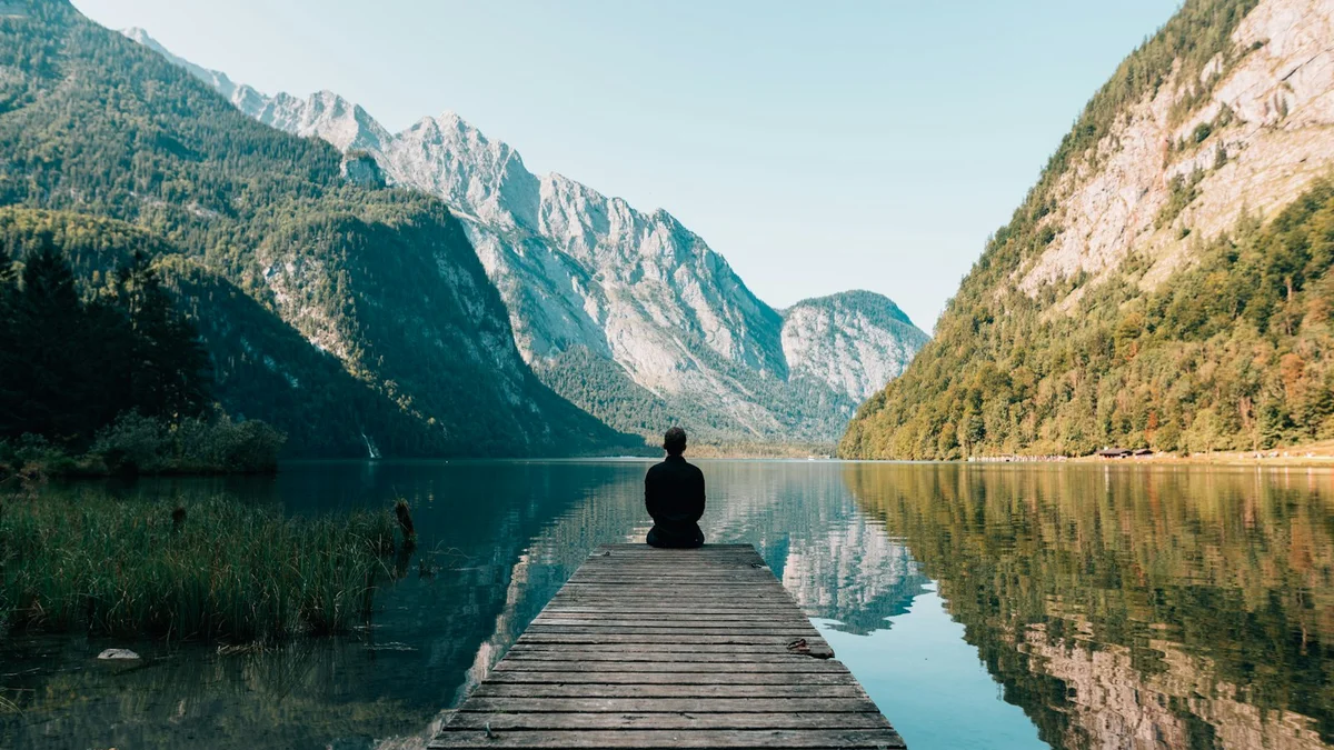 A person sitting alone on a wooden dock over a still alpine lake, mirrored in the calm water with mountains around - a Quiet Core Reset guide to How to Support Burnout Recovery in 10 Minutes a Day.