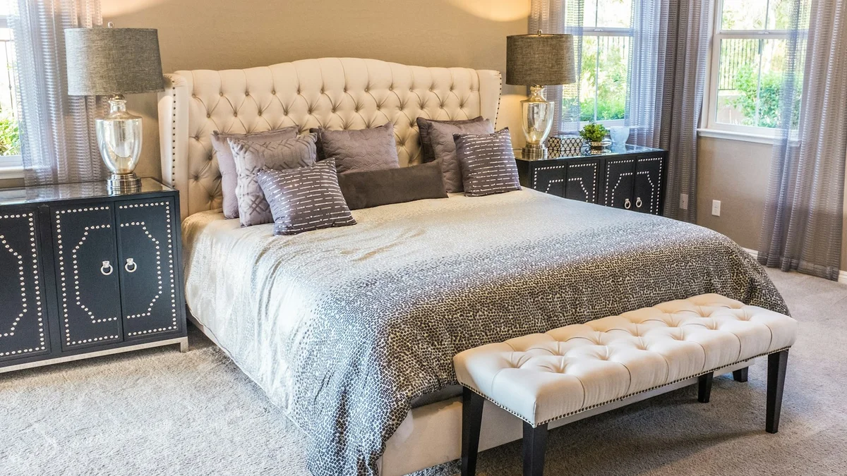A calm, tidy bedroom with a large tufted bed, grey bedding, bedside lamps and soft daylight through windows - a Quiet Core Reset guide to 3-Minute Morning Anchor That Changes Everything.