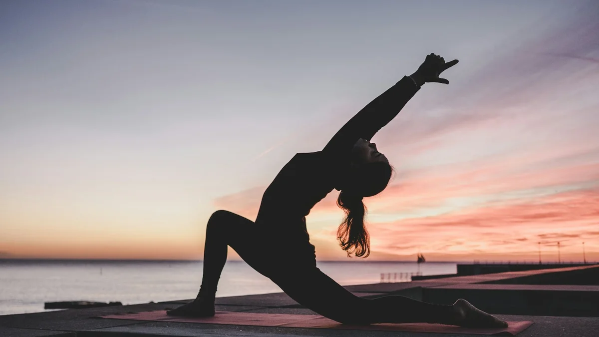 A silhouette of a person in a yoga crescent-lunge pose at sunset over still water, arms reaching up - a Quiet Core Reset guide to 30-Second Shoulder Roll That Changed Everything.