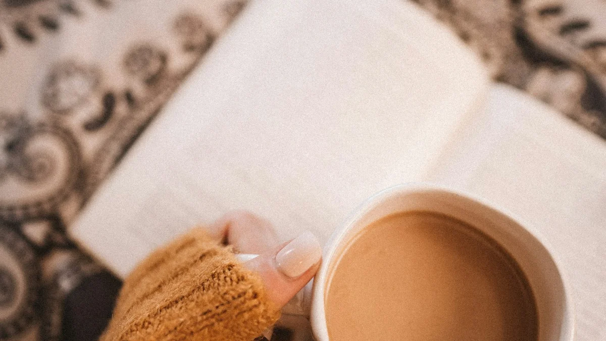 A hand in a knit sleeve wrapped around a warm mug above an open book - a Quiet Core Reset guide to The 60-Second Permission Pause for Rest Guilt.
