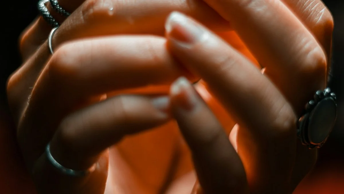 Two hands interlaced and held close in warm amber light, tension resting in the fingers - a Quiet Core Reset guide to The 9 Quiet Signals Your Body Sends Before You Crash.