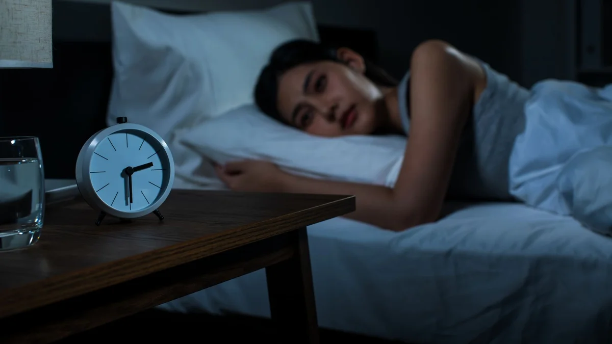 A woman lying awake in bed at night looking toward a glowing bedside clock - a Quiet Core Reset guide to 90-Second Reset for a 3 A.M. Racing Mind.