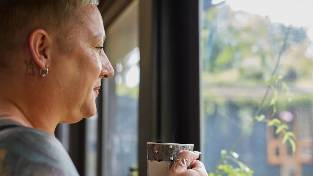 A woman pausing with a mug of coffee by a bright window, soft daylight and greenery outside - a Quiet Core Reset guide to the 90-Second Reframe.