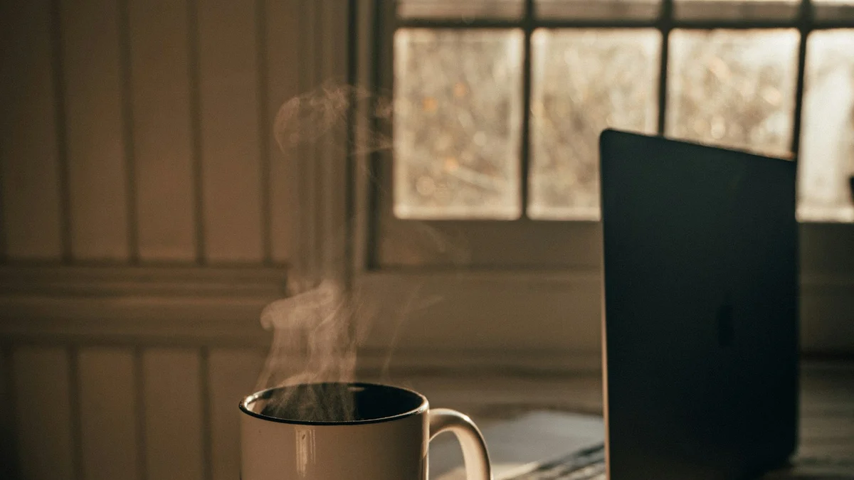 A steaming cup of tea beside a laptop in soft golden window light - a Quiet Core Reset guide to 90-Second Work Energy Reset (Even Mid-Meeting).