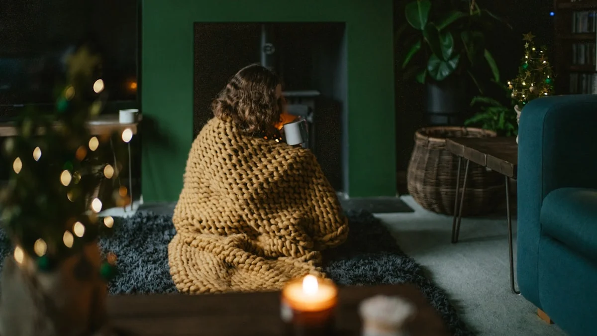 A person wrapped in a chunky blanket resting beside a warm fireplace glow - a Quiet Core Reset guide to High-Functioning Exhaustion When You're Already Burned Out.