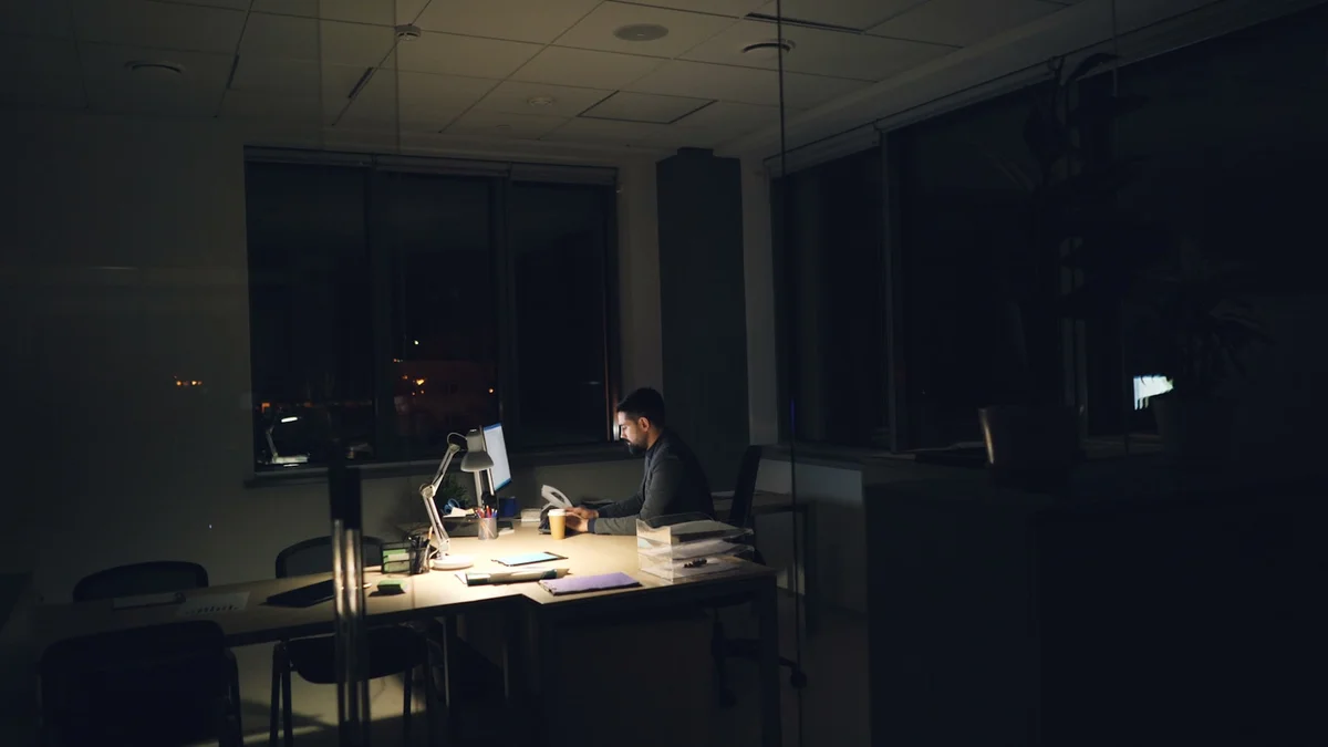 A man working alone at a dimly lit office desk late at night - a Quiet Core Reset guide to Why Always Available Became Normal (and Drains Your Work Energy).