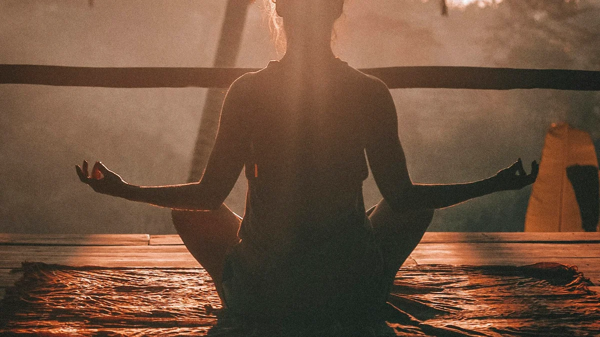 A silhouette seated cross-legged in a meditation pose, hands resting on the knees, backlit in warm golden light - a Quiet Core Reset guide to Beginner's Guide to Entering Rest & Digest.