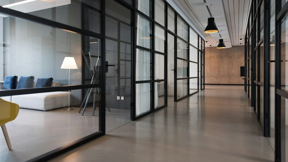 A modern glass-walled office corridor with a lounge area, black frames and warm pendant lights - a Quiet Core Reset guide to Beginner's Guide to Gentle Space-Creation.