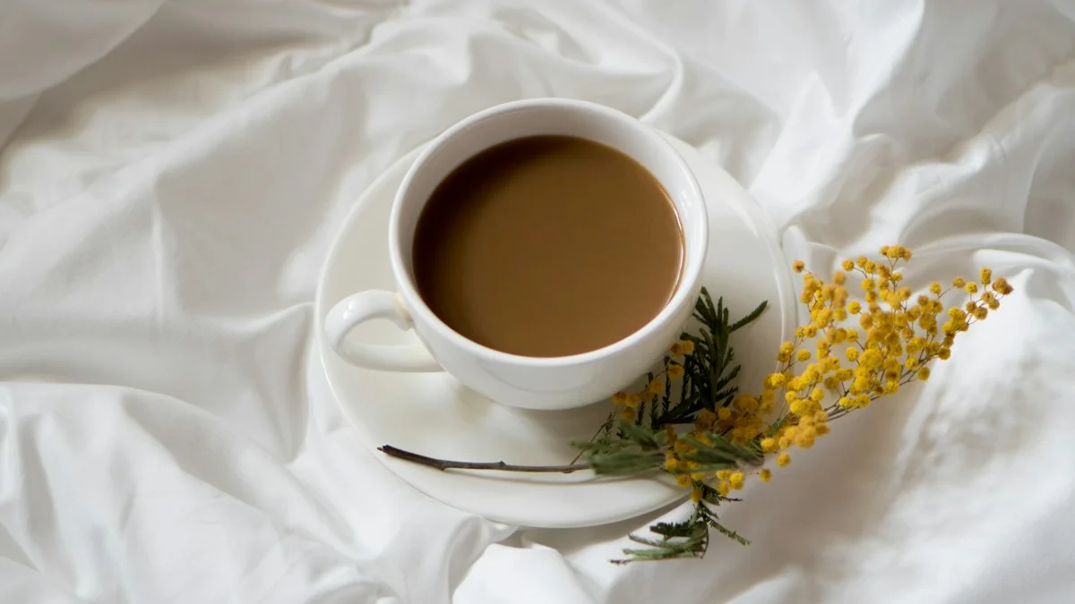 A full cup of tea on a white saucer with a sprig of yellow mimosa on soft linen - a Quiet Core Reset guide to Setting Boundaries Explained Simply (No Jargon, No Guilt).