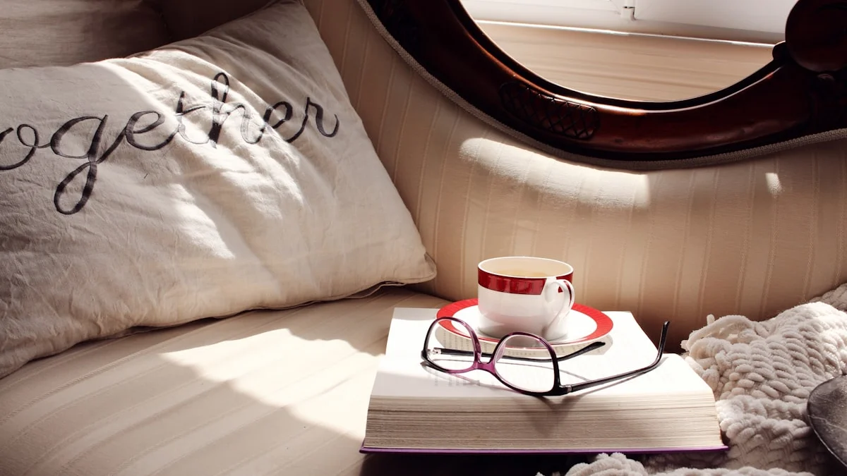 An open book with reading glasses and a cup of tea rest on a sunlit cosy sofa - a Quiet Core Reset guide to Boundaries for Low-Energy Days: 'No' Is the Gentle Minimum.