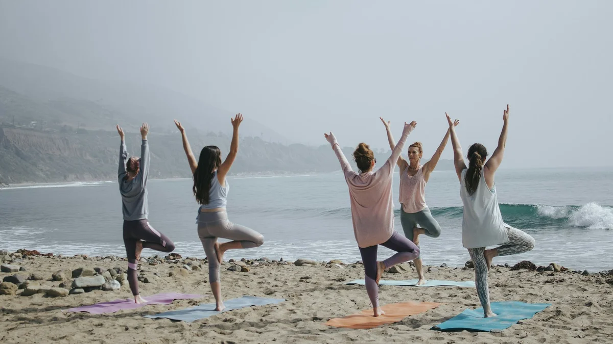 A group of women doing a standing yoga pose on a beach at sunrise with the ocean behind - a Quiet Core Reset guide to Breathing Techniques.