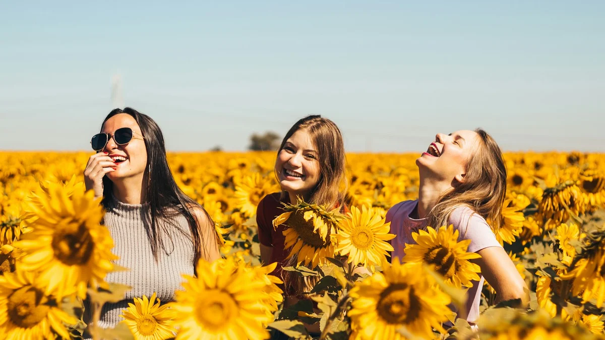 Three women laughing joyfully in a sunflower field on a bright sunny day - a Quiet Core Reset guide to Breathing for Parents & Caregivers.