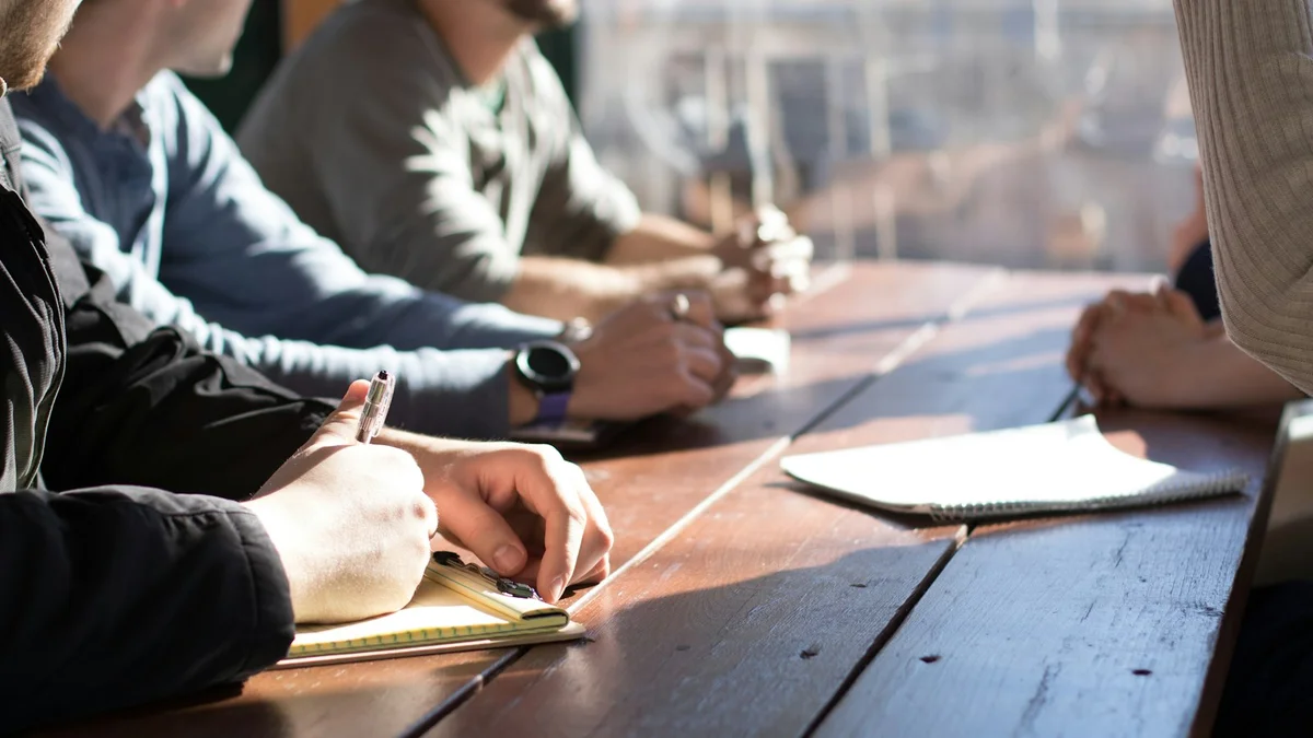 Hands writing in a notebook at a long wooden table, a group workshop in warm light - a Quiet Core Reset guide to Breathing for High Performers.