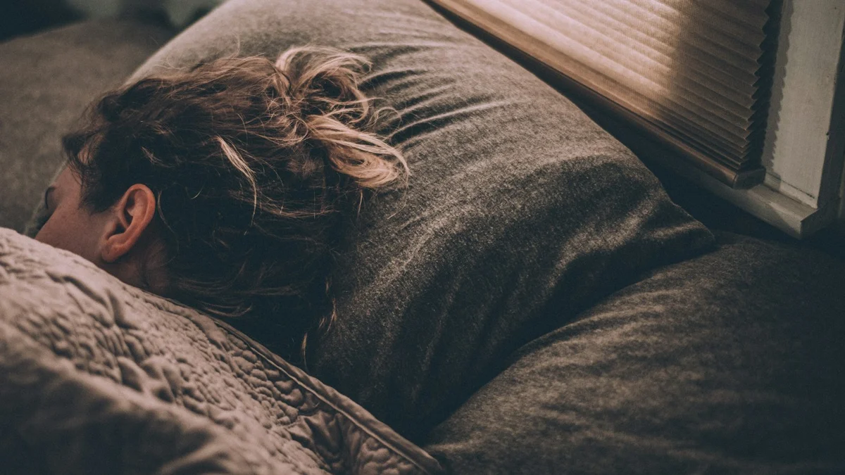 A person lying awake in a dark bed at night, face turned into the pillow - a Quiet Core Reset guide to Why You Can't Wind Down at Night Anymore (It's Not Your Discipline).