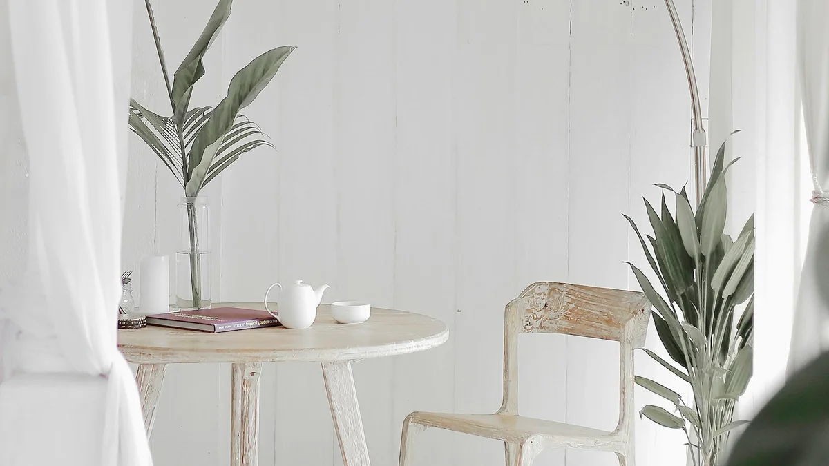 A bright minimal room with a white table, a teapot and cup, a book and green plants - a Quiet Core Reset guide to Coming Home to Yourself.