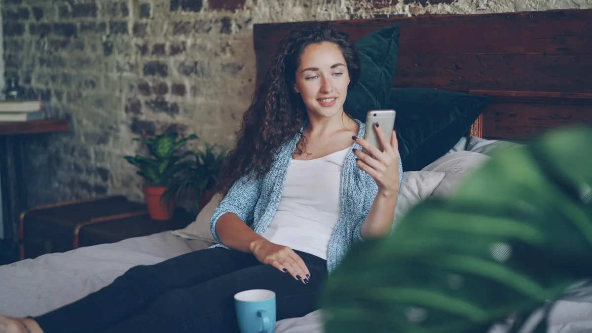 A woman sitting on her bed in a warm rustic room, scrolling her phone beside a mug - a Quiet Core Reset guide to Comparison and FOMO: 12 Questions, Answered.