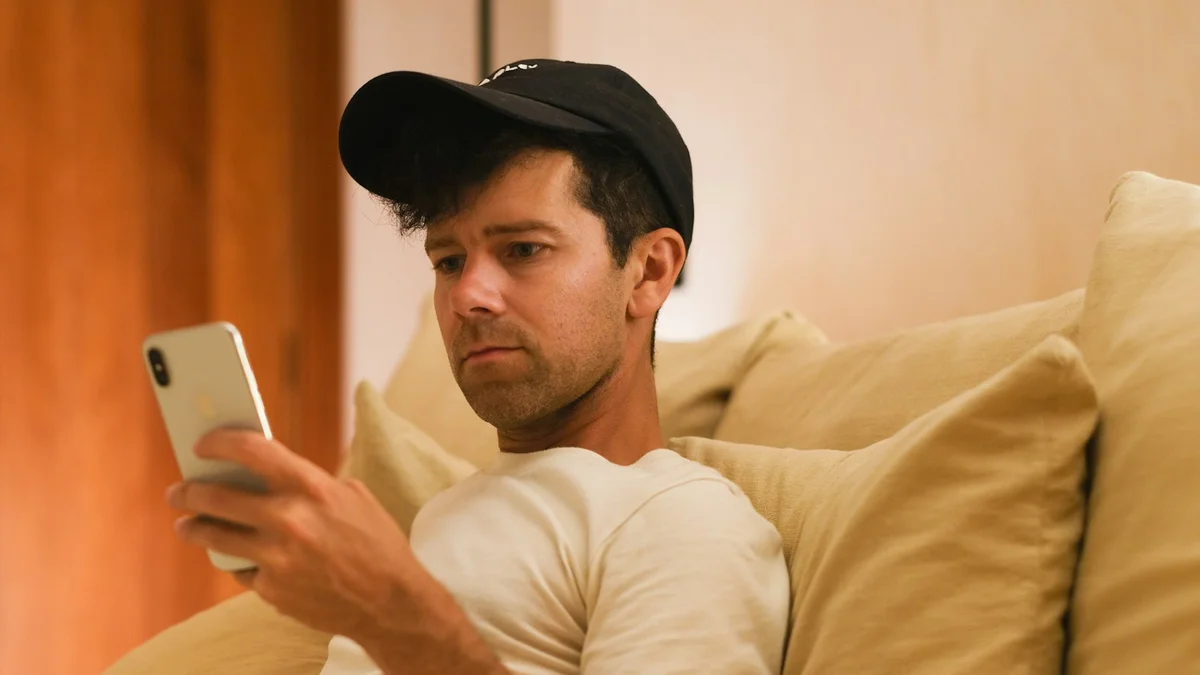 A tired man slumped against couch cushions scrolling his phone in low warm light - a Quiet Core Reset guide to Low-Energy Days: When the Feed Feels Heaviest.