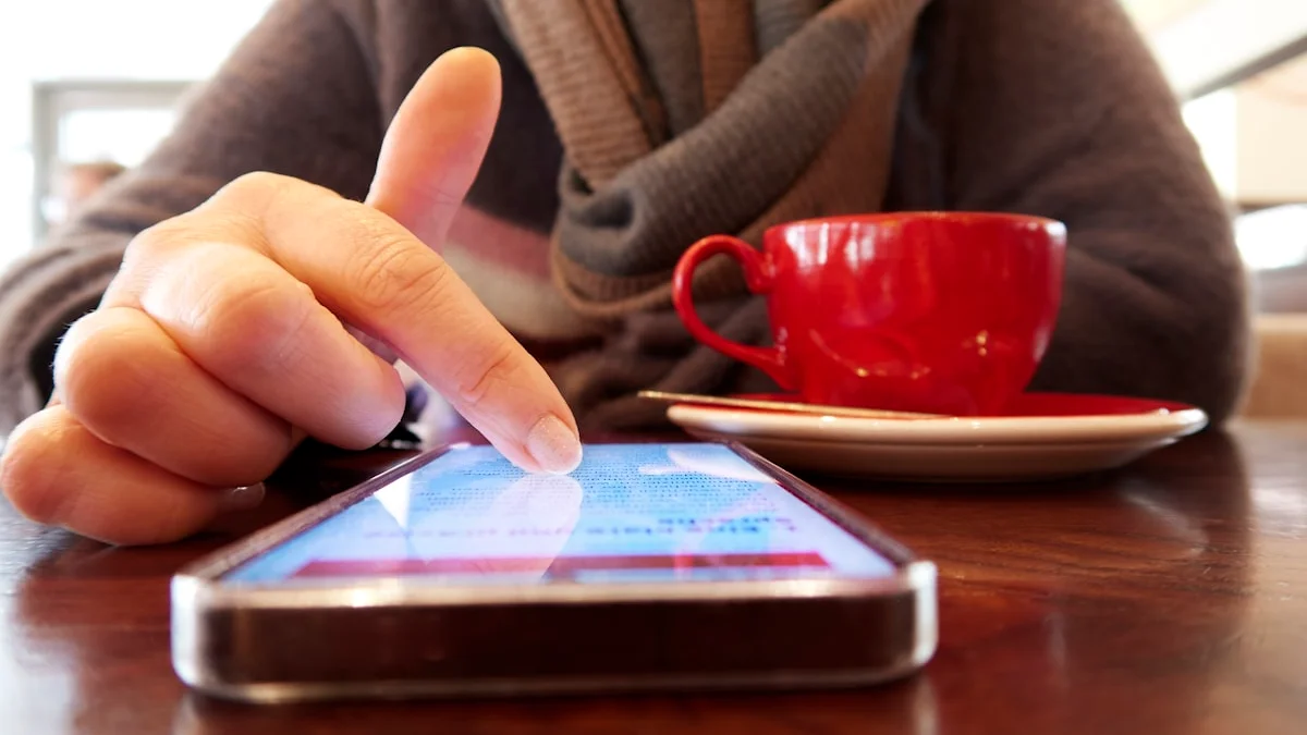 A hand scrolling a smartphone beside a red cup of coffee in warm light - a Quiet Core Reset guide to The Comparison Trap.
