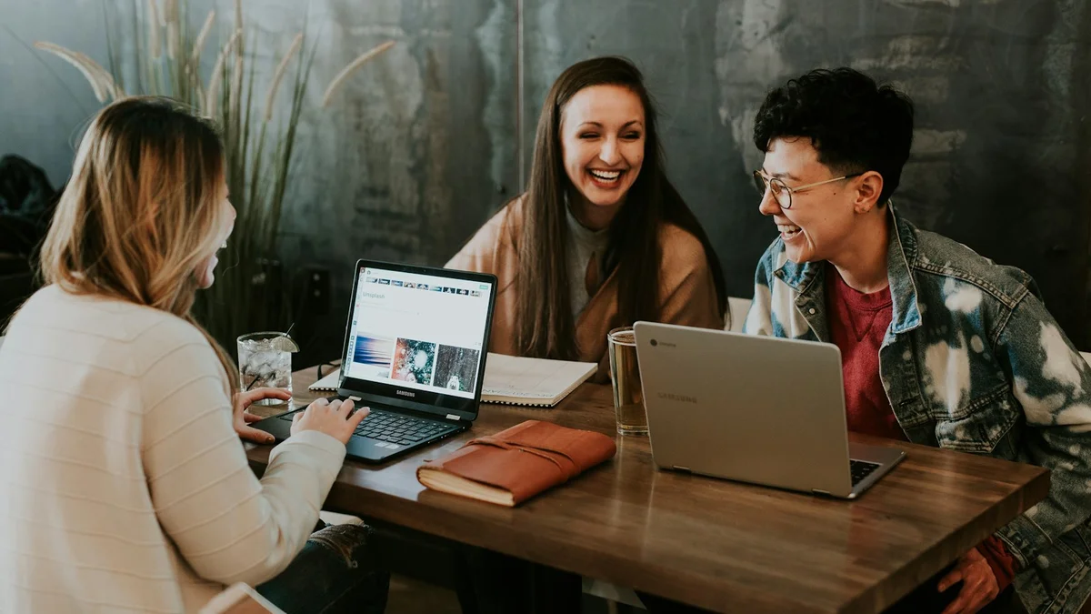 Three people laughing together at a table with laptops and notebooks, a casual meeting - a Quiet Core Reset guide to Depleted at Work.