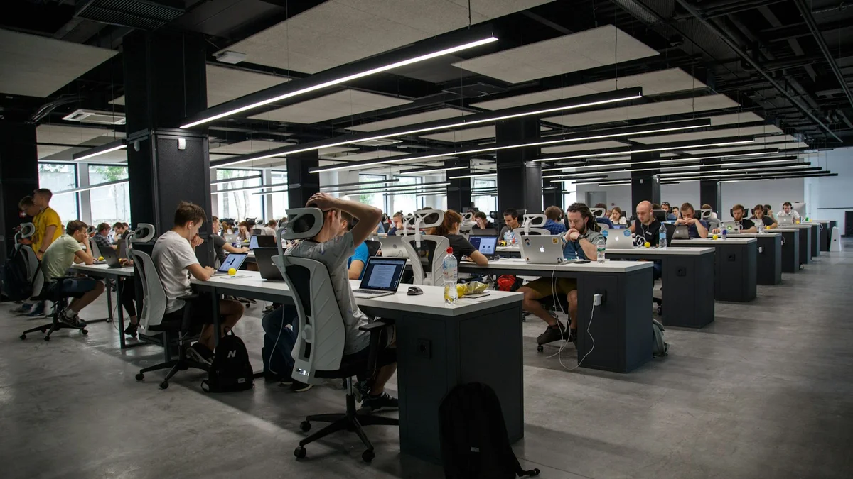 A large open-plan office with rows of desks, people working at laptops under long suspended lights - a Quiet Core Reset guide to Depletion for High Performers.
