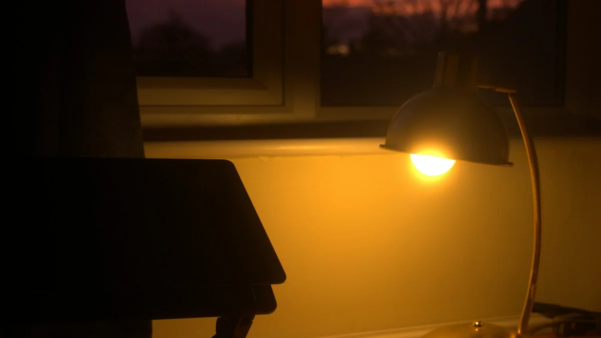 A desk lamp glowing against the sunset beside a darkened laptop - a Quiet Core Reset guide to How to End Your Workday.