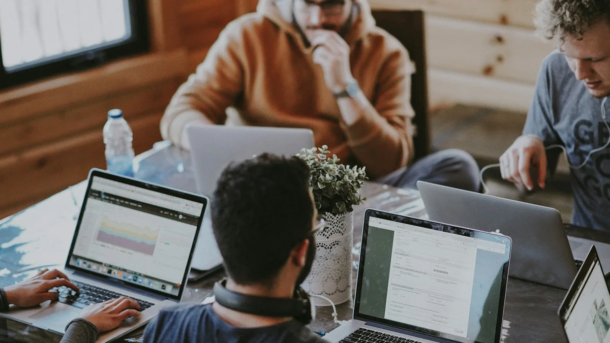 A group of people working at laptops around a table with a small plant, a busy co-working session - a Quiet Core Reset guide to Energy Management for Freelancers.