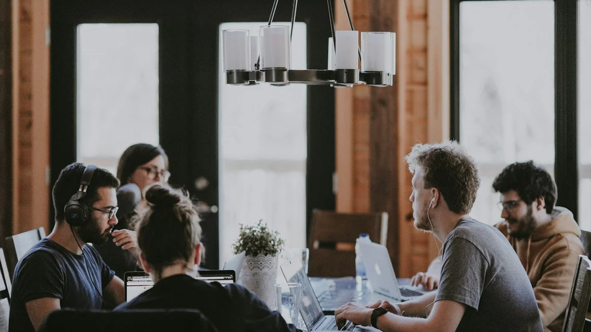 A group of people working on laptops at a long table in a shared office - a Quiet Core Reset guide to Energy-Giving vs. Energy-Taking Activities.