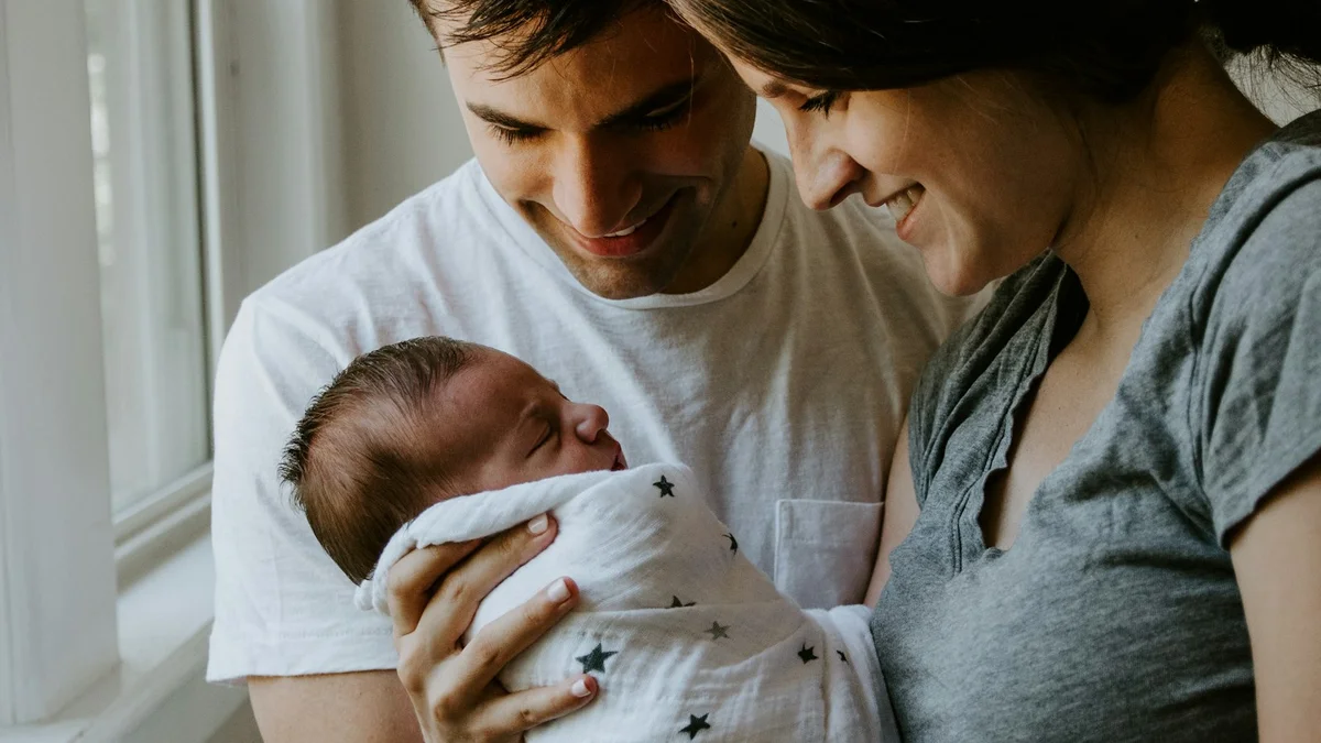 A couple smiling and holding a newborn baby wrapped in a swaddle, warm and close - a Quiet Core Reset guide to Energy Management for Parents.