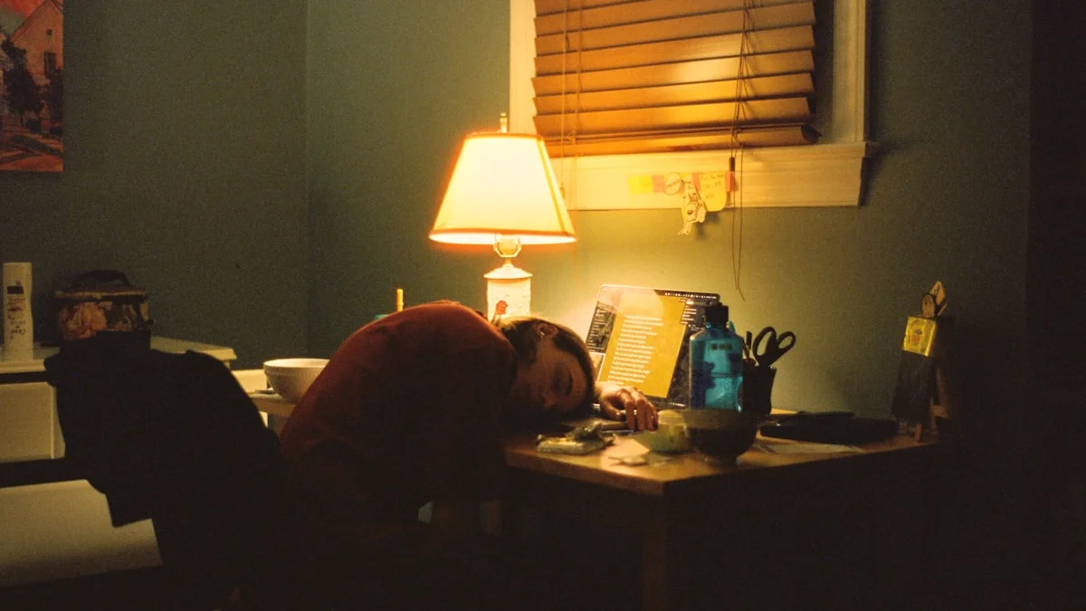 An exhausted worker slumps at a cluttered desk under a warm lamp late at night - a Quiet Core Reset guide to 7 Ways to Protect Your Energy at Work When You're Quietly Exhausted.
