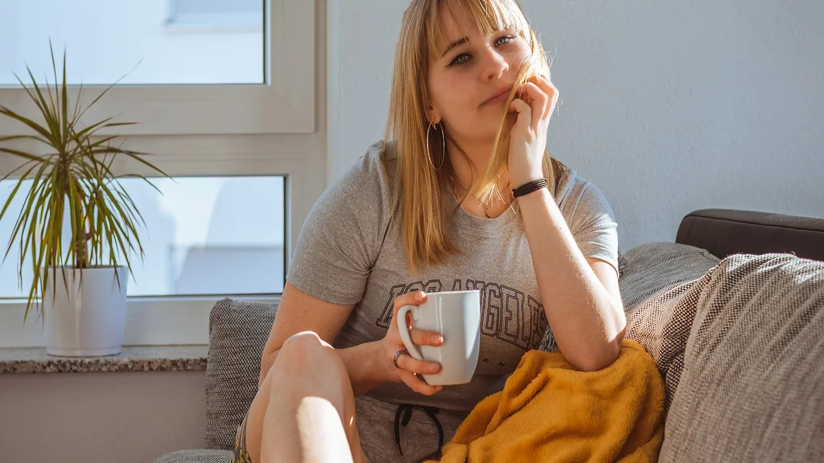A woman resting on the couch under a yellow blanket with a warm mug - a Quiet Core Reset guide to Family Energy When You're Already Burned Out.