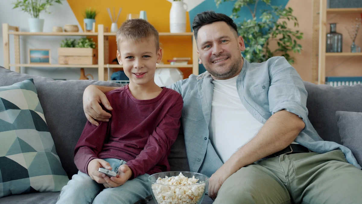 A father and son relaxing together on the couch with a bowl of popcorn - a Quiet Core Reset guide to Family Energy Explained Simply.