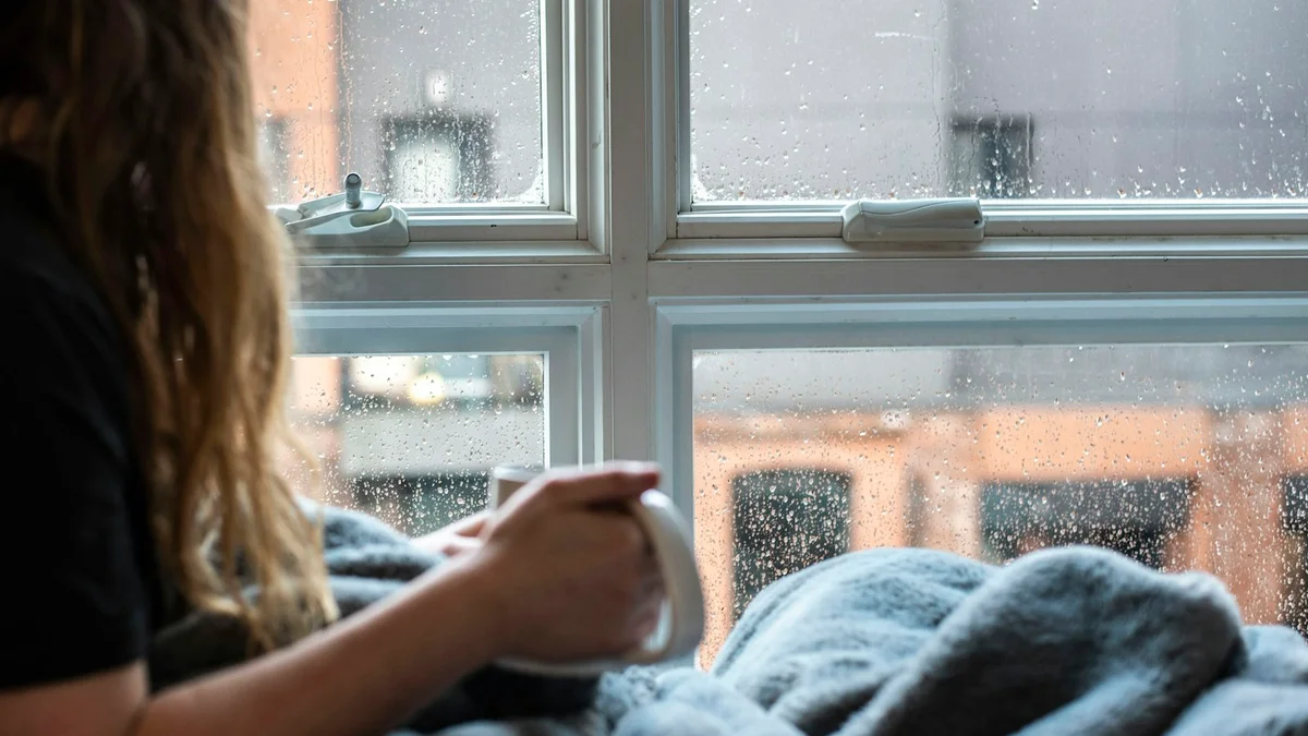 A woman wrapped in a blanket holding a warm mug beside a rain-streaked window - a Quiet Core Reset guide to Already Burned Out? Why You Feel Like You're Not Enough.
