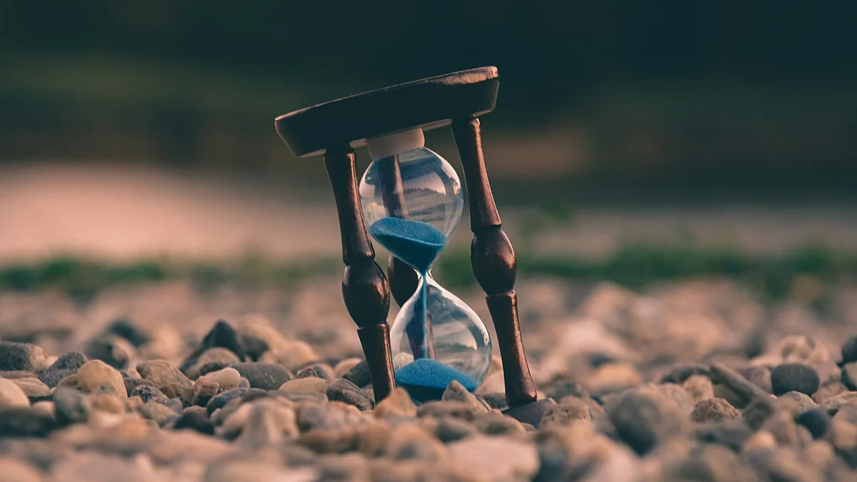 A wooden hourglass with blue sand resting on pebbles, a quiet symbol of time passing - a Quiet Core Reset guide to Hidden Energy Leaks in Your Day.