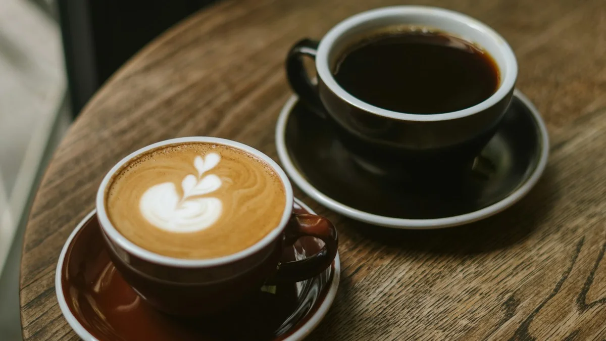 A latte and a black coffee sitting side by side on a round wooden cafe table - a Quiet Core Reset guide to Myths About High-Functioning Exhaustion, Debunked.