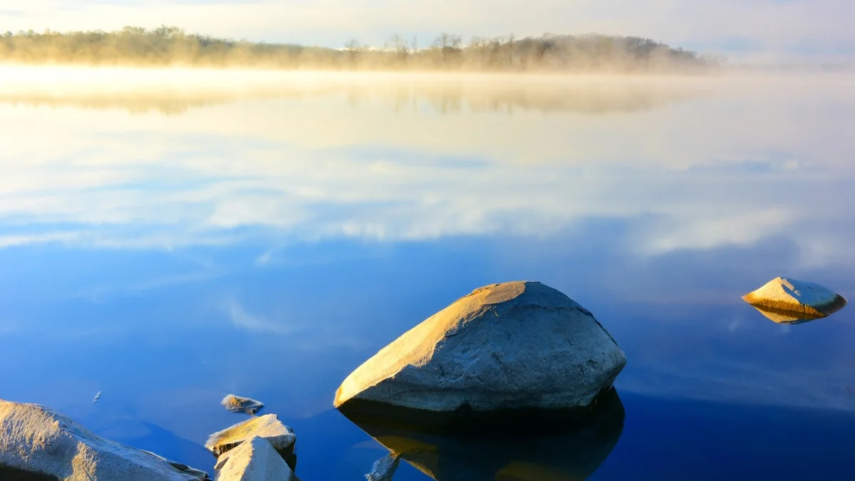 Soft morning mist drifting over a still lake at sunrise, smooth rocks resting in the calm water - a Quiet Core Reset guide to How to Stop Fighting Your Own Feelings.