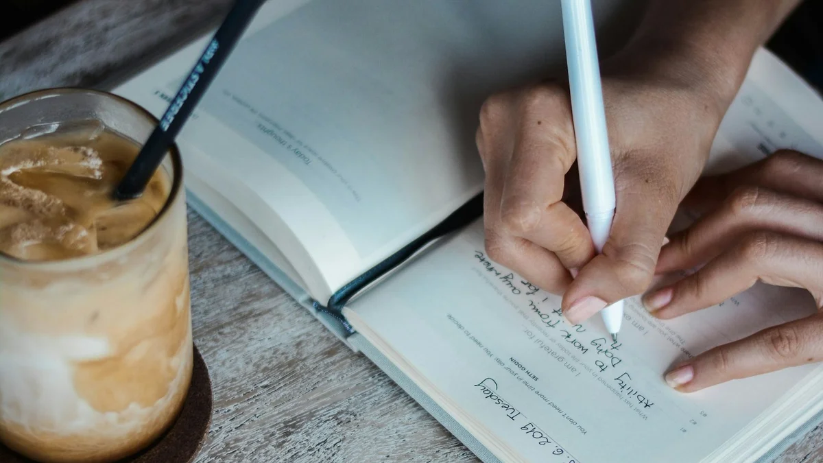 Hands writing in an open journal beside a coffee on a warm wooden table - a Quiet Core Reset guide to Beginner's Guide to Quieting Your Inner Critic.
