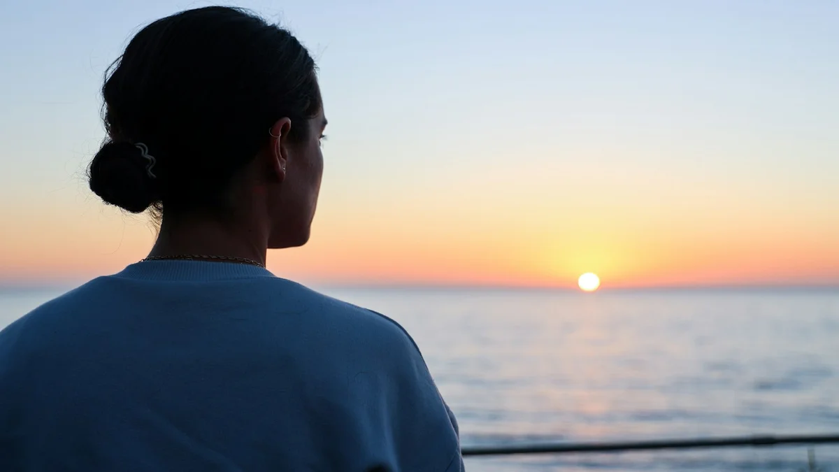 A woman gazing at the sunrise over a calm sea - a Quiet Core Reset guide to How High Performers Quiet the Inner Critic (Without Losing Drive).
