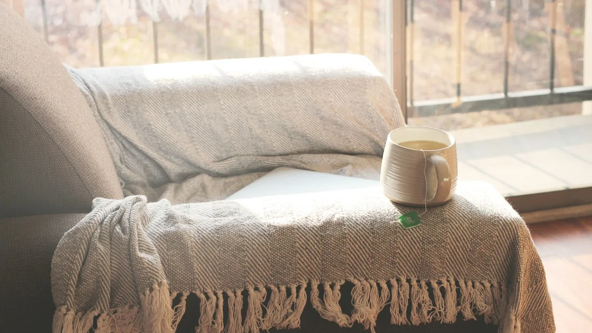 A cup of tea on an armchair beside a window with a draped blanket - a Quiet Core Reset guide to Self-Talk for Low-Energy Days.