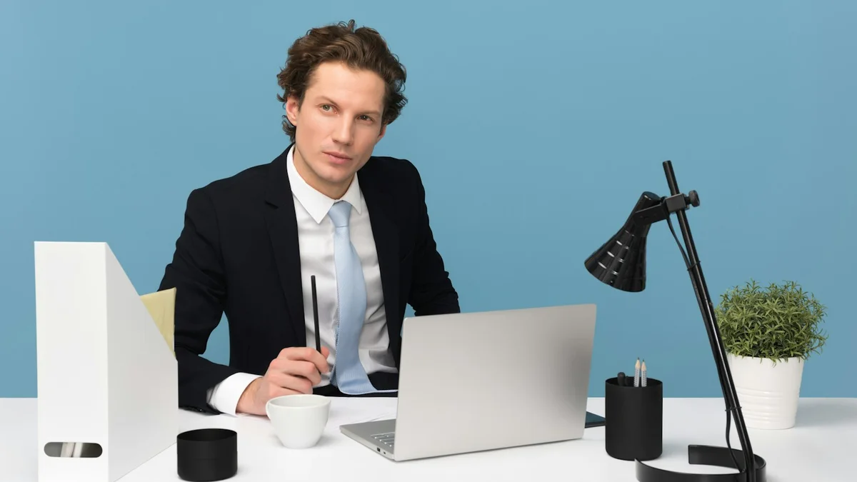 A man in a suit at a desk with a laptop and lamp, a business portrait against a blue wall - a Quiet Core Reset guide to How I Learned What Real Rest Feels Like.
