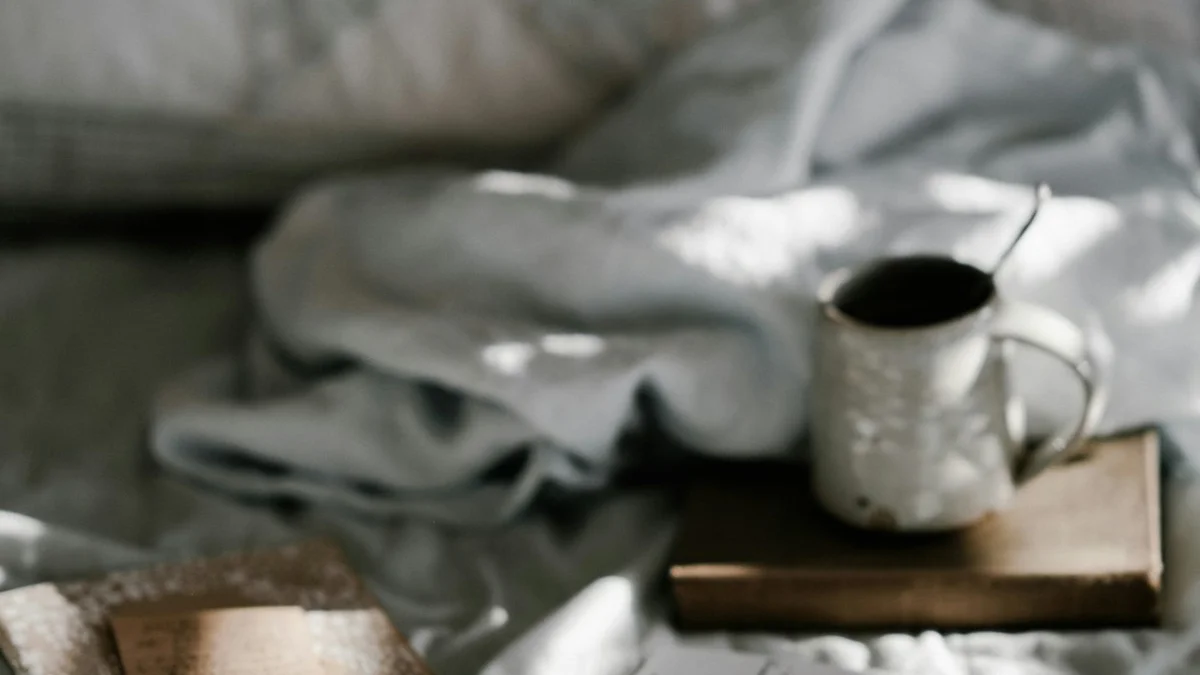 A coffee mug resting on a worn book beside an open journal in soft morning light on an unmade bed - a Quiet Core Reset guide to Subtle Ways You’ve Lost Your Slowness.