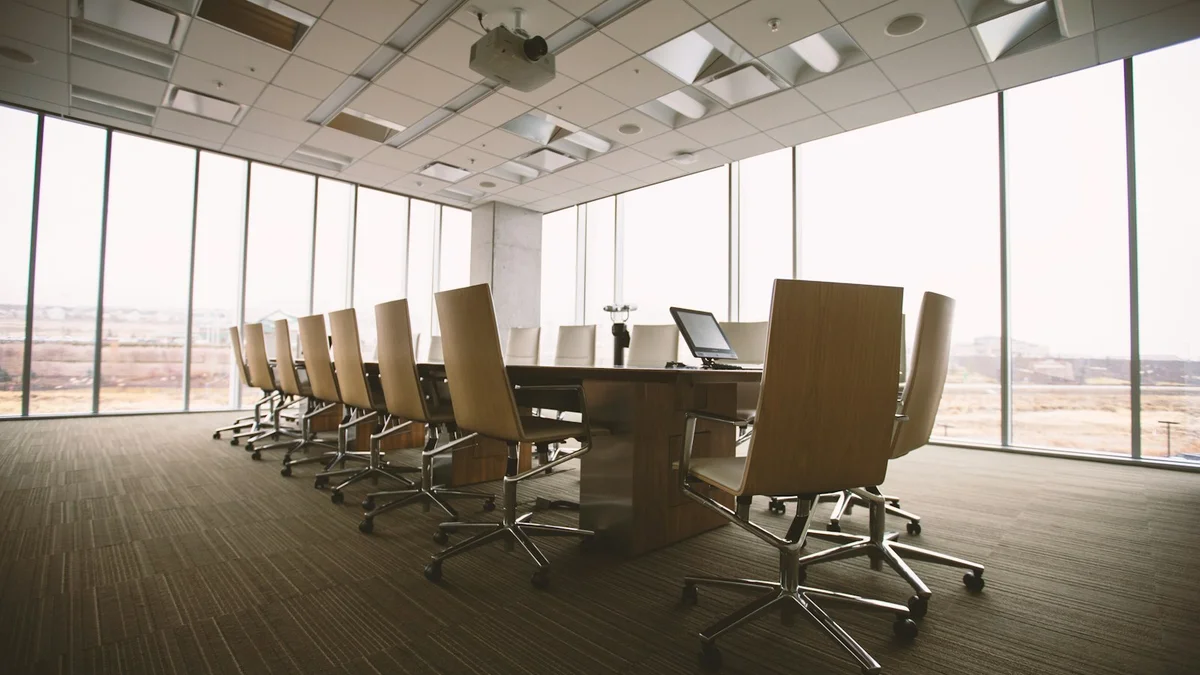 An empty meeting room with chairs around a long table by large windows - a Quiet Core Reset guide to Why Meetings Drain You More Than Hard Work (and What Helps).
