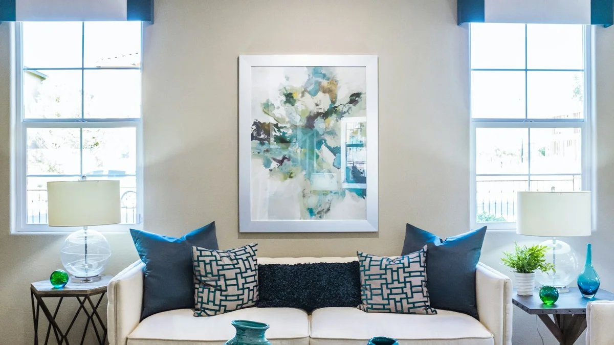 A living room with a sofa, blue pillows, a large abstract painting and two windows - a Quiet Core Reset guide to Micro-Resets When You're Already Burned Out.