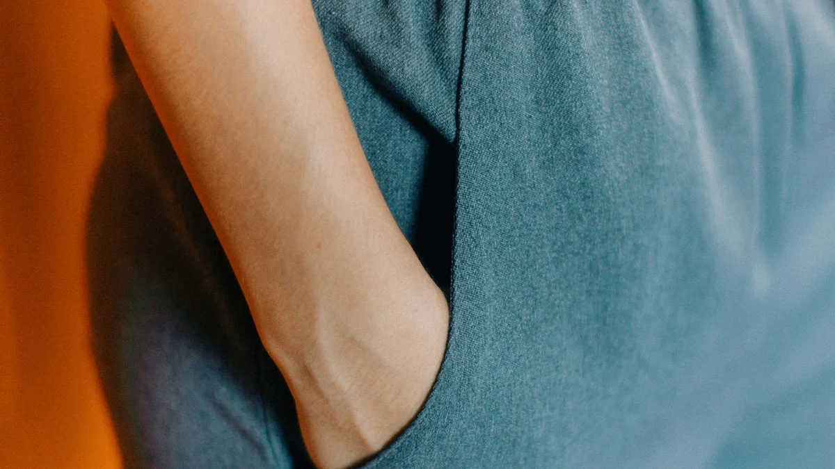 A hand resting against a person's blue clothing, a soft orange background - a Quiet Core Reset guide to Micro-Resets Explained Simply.