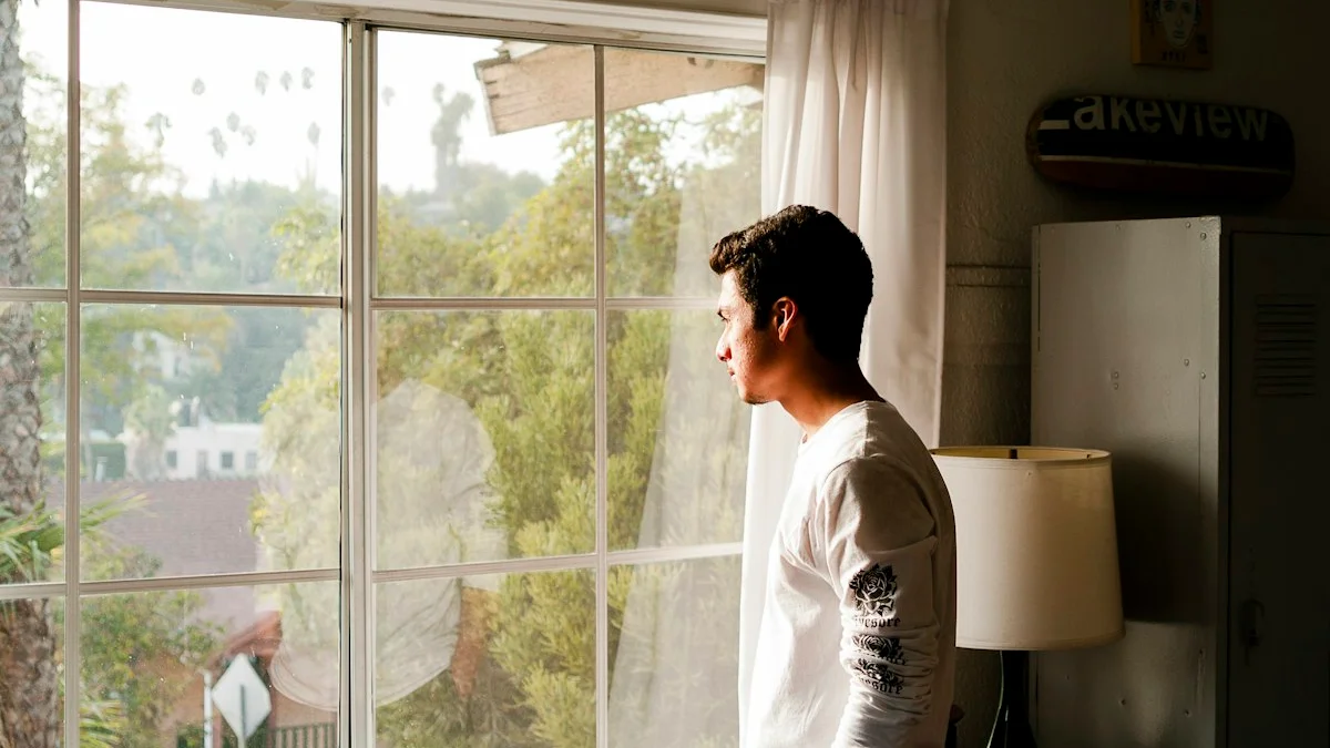 A man standing at a sunlit home window, gazing out at the trees, lost in thought - a Quiet Core Reset guide to Mind Reading.