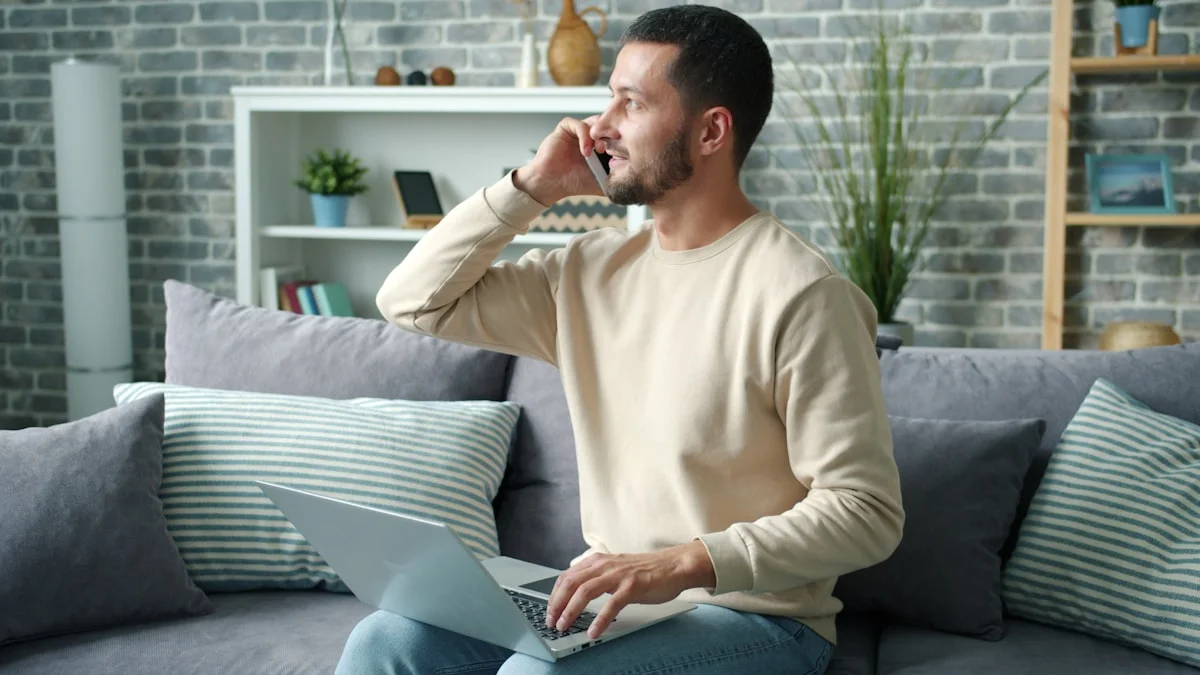 A man taking a phone call while typing on a laptop balanced on his lap, doing two things at once - a Quiet Core Reset guide to Why Multitasking Is Making You More Tired.
