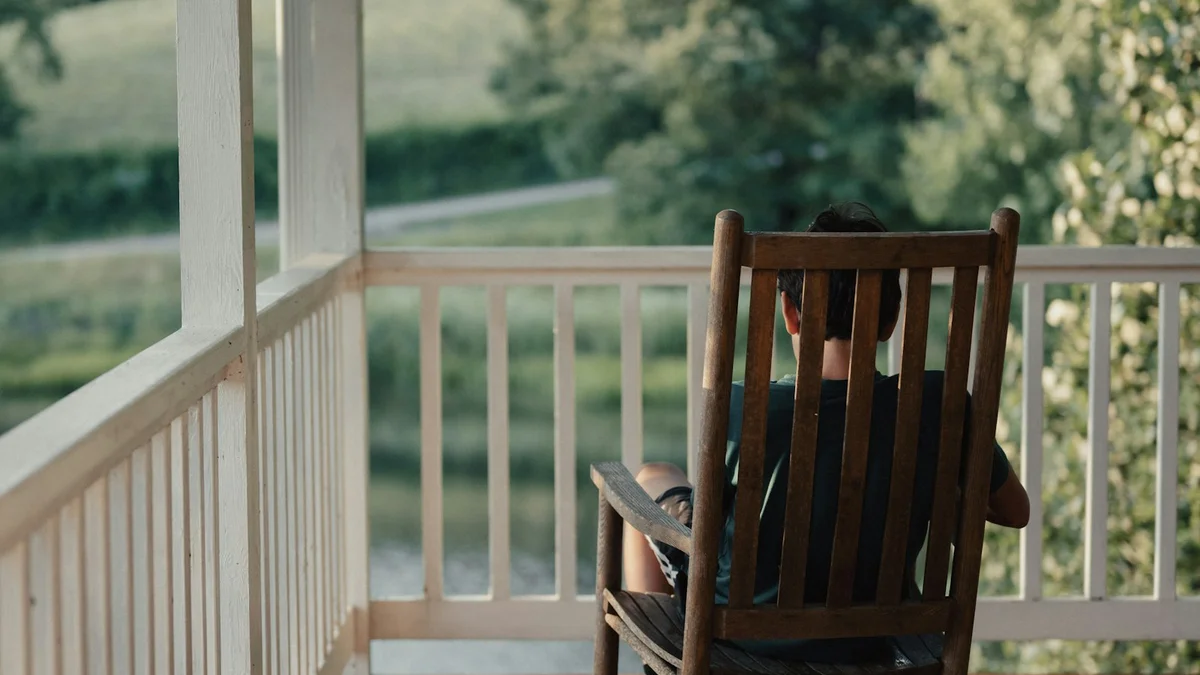A person sitting in a wooden rocking chair on a porch, looking out over green hills - a Quiet Core Reset guide to How I Unlearned My Worth Is My Output (and Started Resting).