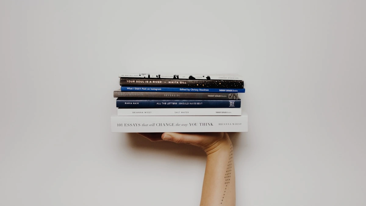 A hand holding up a neat stack of well-read books against a plain wall - a Quiet Core Reset guide to Nervous System Regulation.