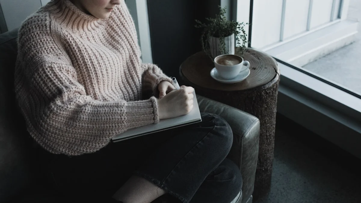 A woman in a chunky knit sweater journals in a leather armchair by a bright window, coffee on a wooden side table - a Quiet Core Reset guide to Nervous System Regulation for Low-Energy Days.