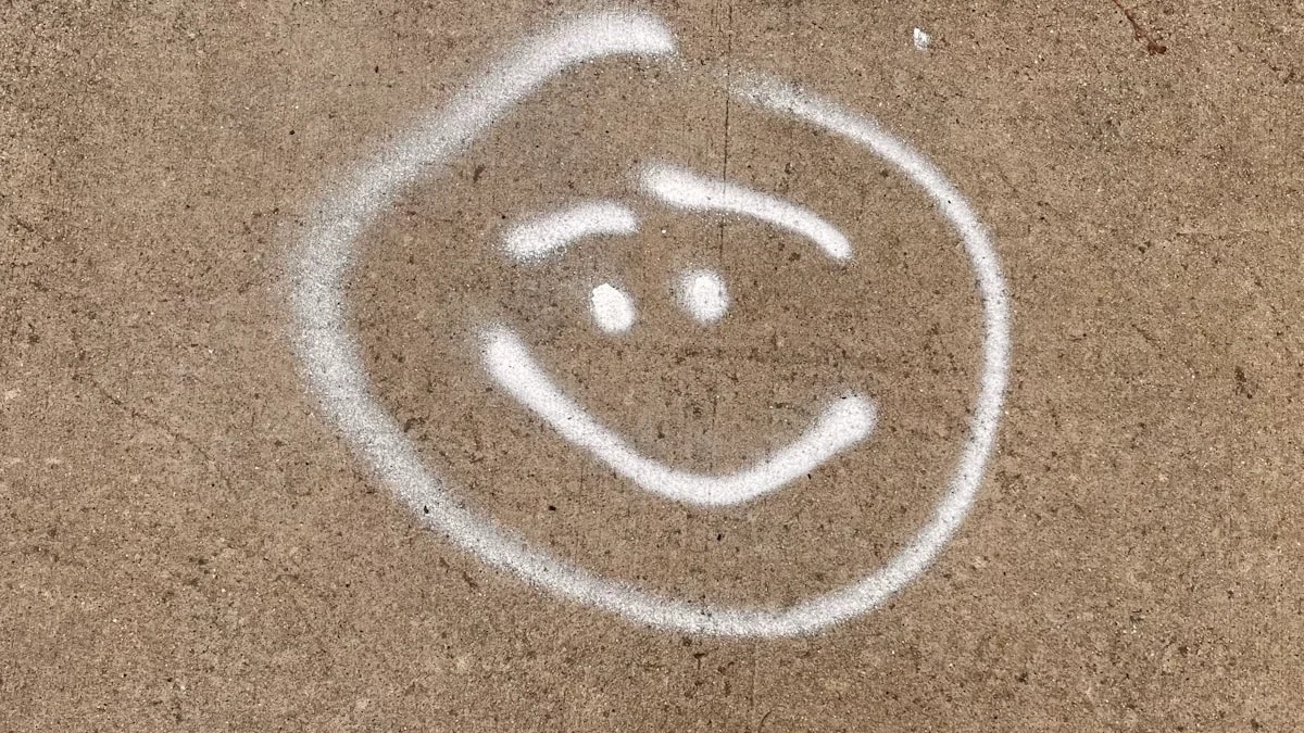 A faded smiley face spray-painted on grey concrete, cheerfulness sketched onto a hard surface - a Quiet Core Reset guide to Overcoming Toxic Positivity.