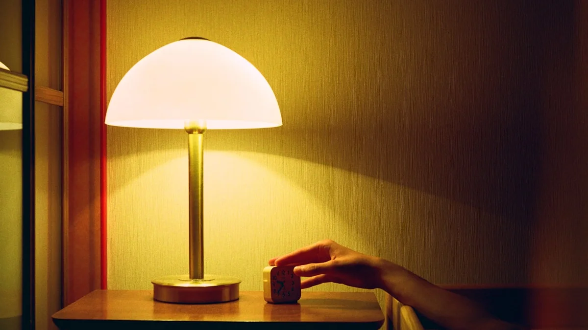 A hand reaching to silence an alarm clock beside a glowing bedside lamp in a dim, warm room at night - a Quiet Core Reset guide to Overstimulation.
